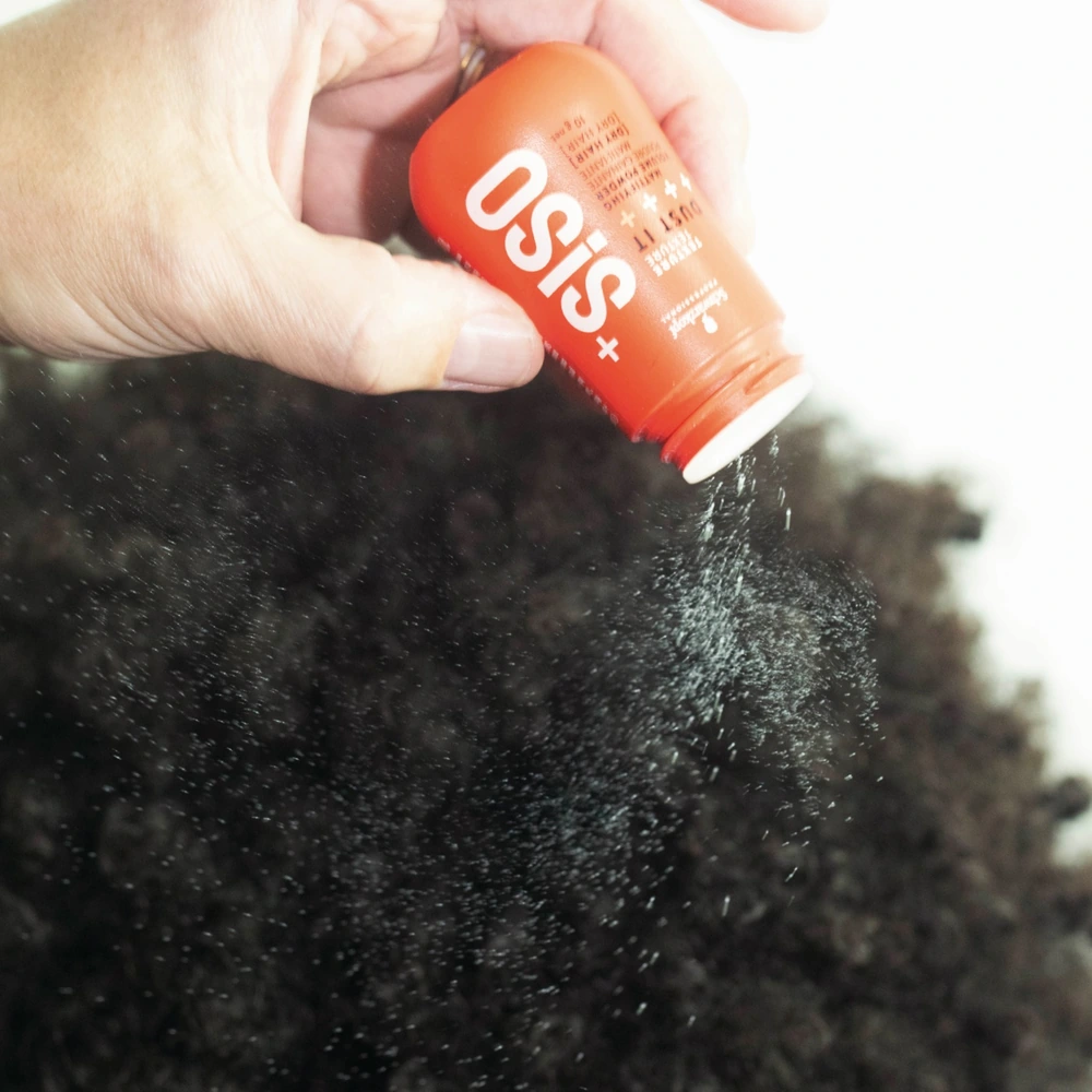 Une main verse de la poudre Dust It sur des cheveux crépus, sur une photographie du fabricant.