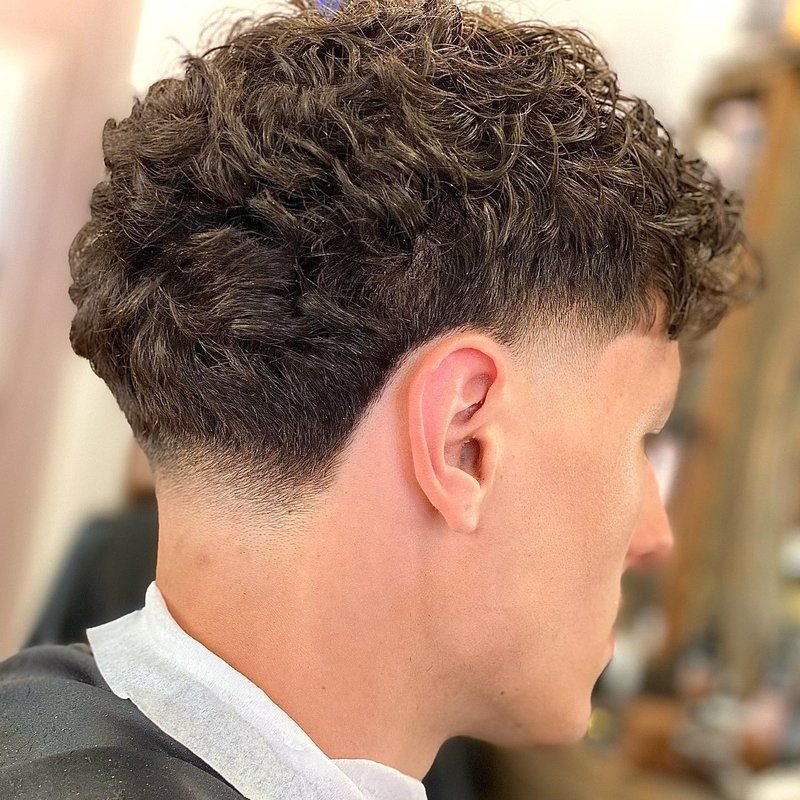 Trois quarts arrière d’un homme aux cheveux bouclés châtains, montrant la nuque et la tempe dégradées.