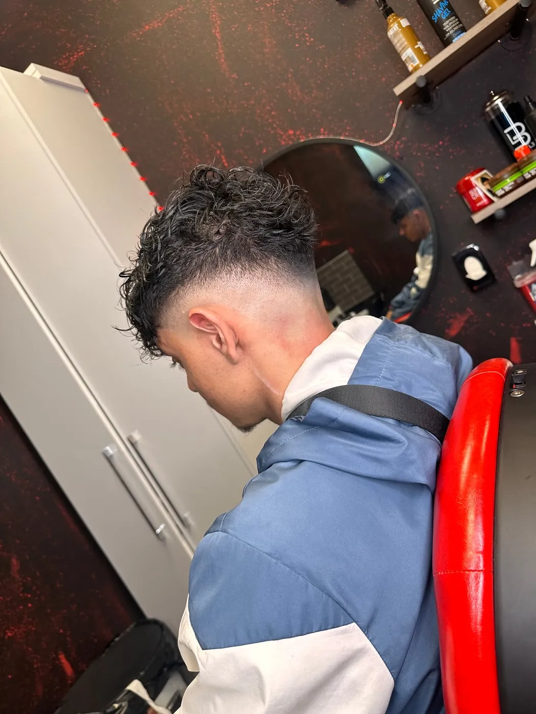 Trois quarts arrière d’un mid skin fade avec boucles sur le dessus et bande très courte continue autour de l’oreille et de la nuque.
